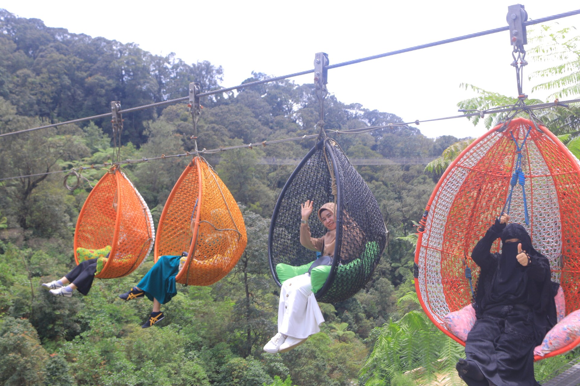 Visitors riding the colorful Keranjang Sultan woven wicker pods gliding high across the valley at Kawah Rengganis Ciwidey
