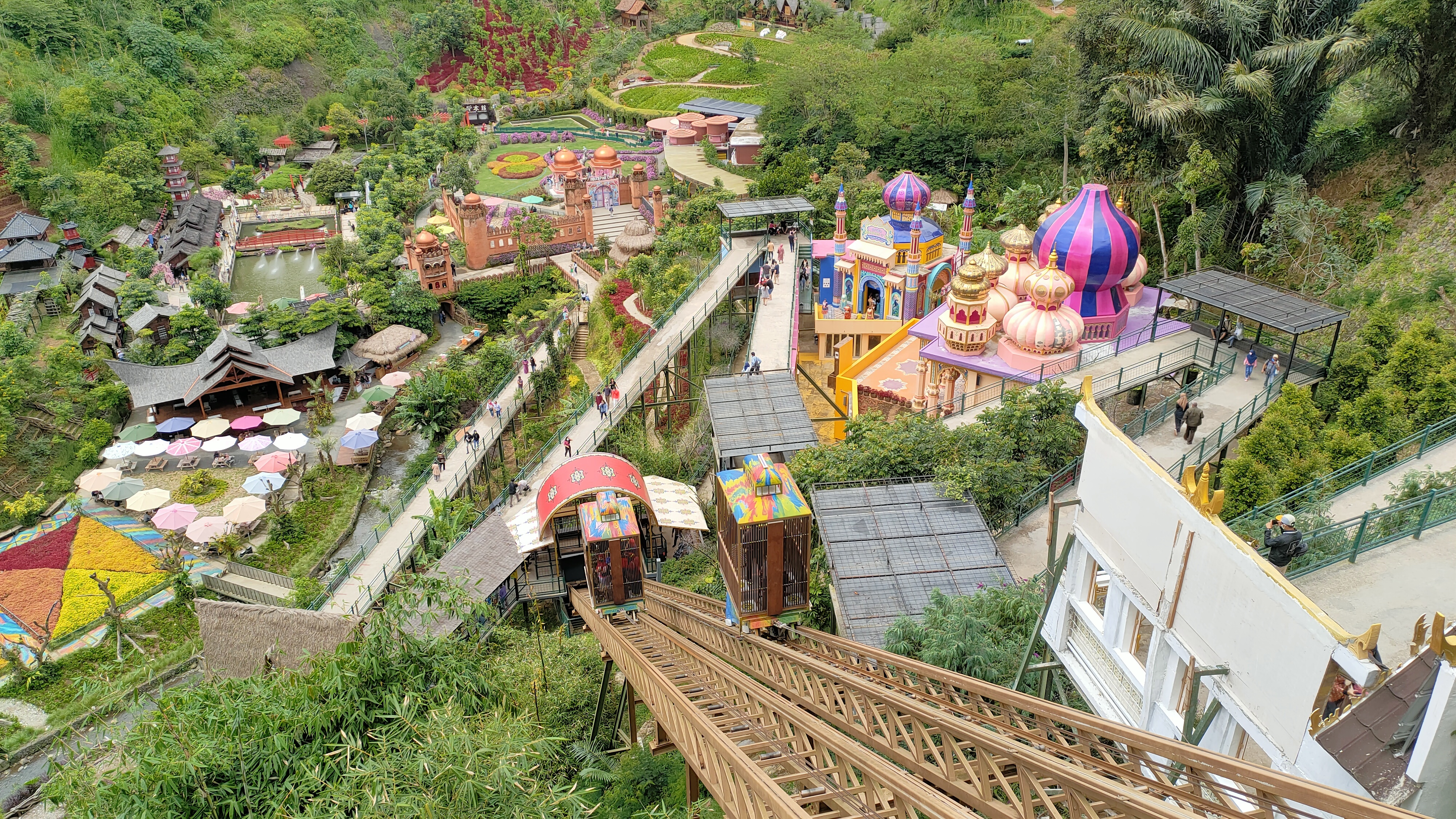 Panoramic valley view of The Great Asia Africa Lembang with colorful cultural pavilions, incline gondola lift, and lush green hills